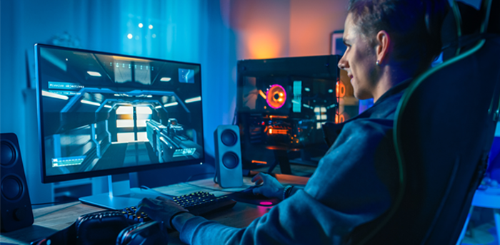 Homem branco sentado em frente à tela de um PC gamer se diverte com um jogo, aproveitando a segurança em decorrência do uso de nobreak.